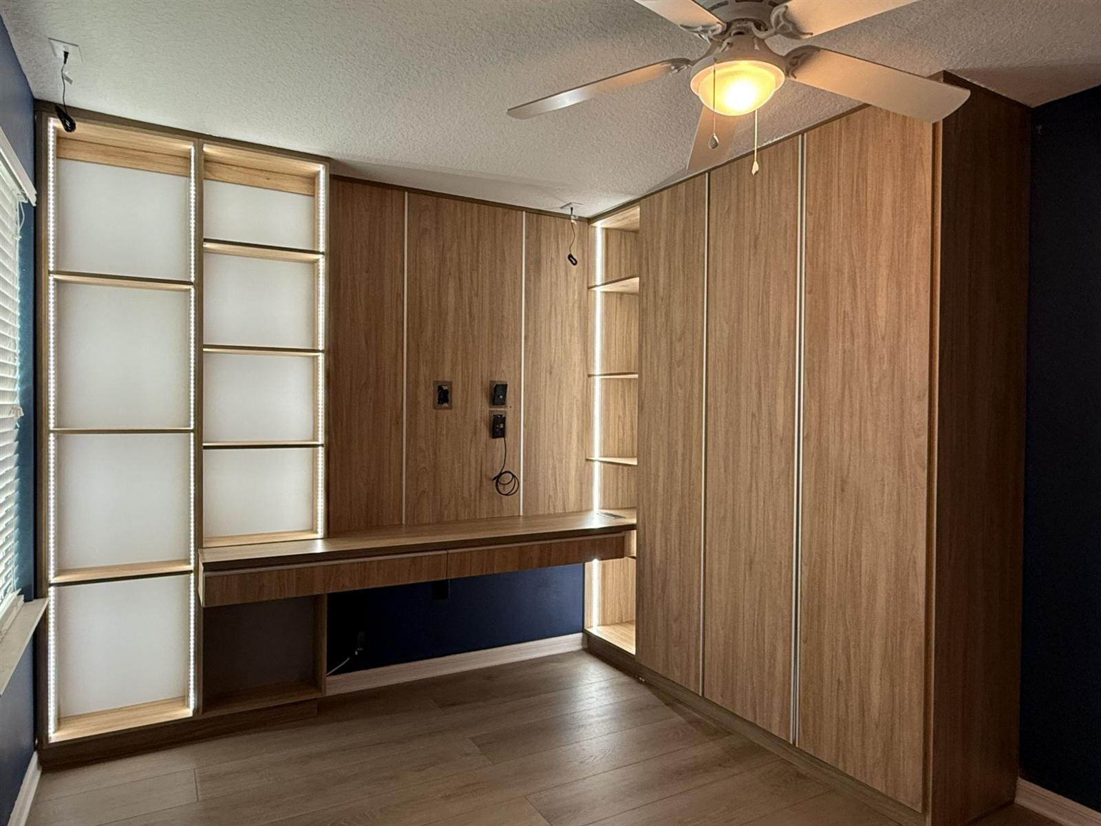 Custom wood-tone home office built-in with LED shelving, floating desk and tall wardrobe, built by Karino Custom Closets in Orlando FL